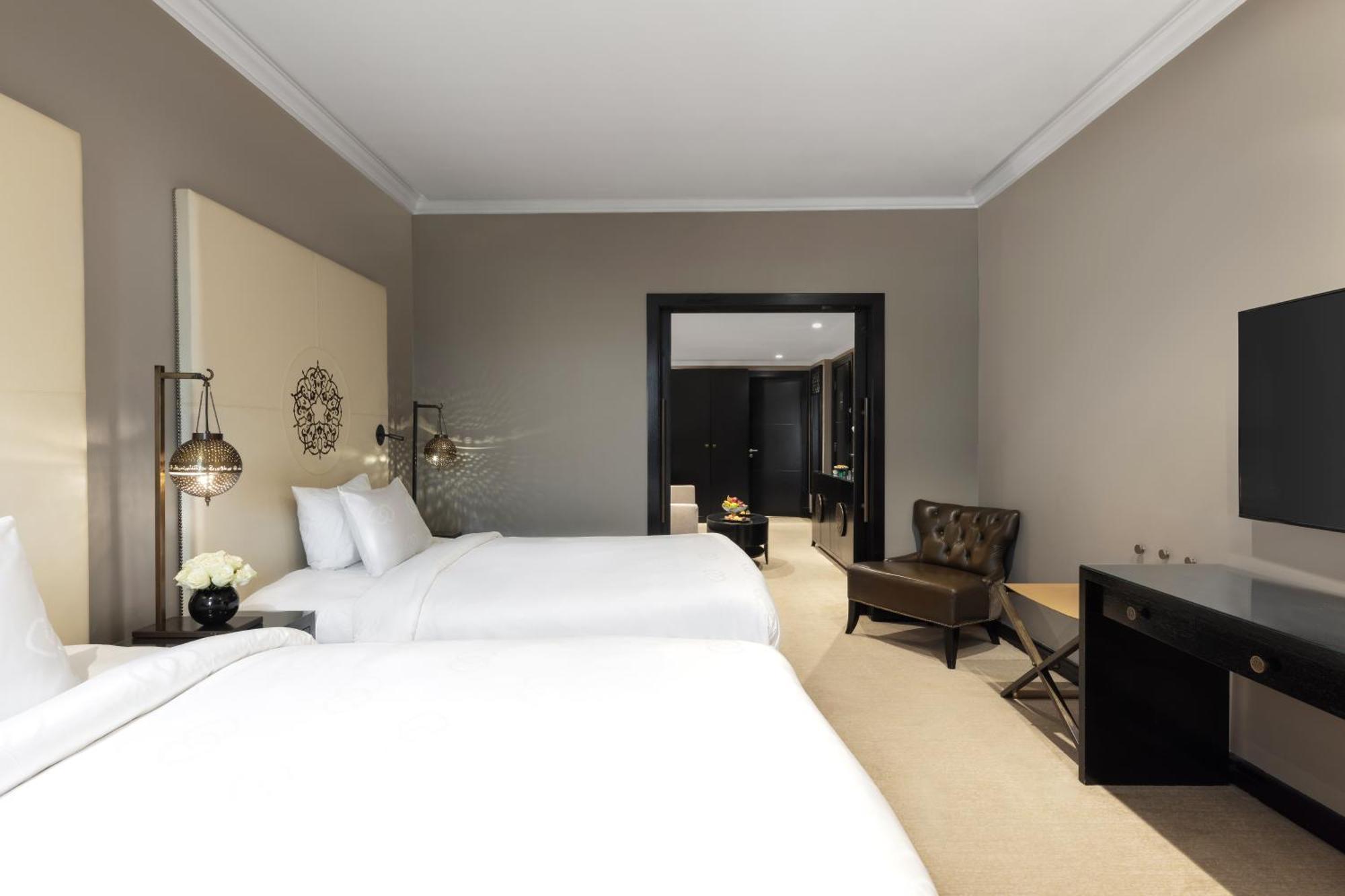 Готель Sofitel Shahd Al Madinah Medina Екстер'єр фото The photo shows a hotel room with a modern design. It features two white beds with neatly arranged pillows, a simple beige wall with decorative accents, and stylish bedside lamps. There is a small seating area with a brown chair and a side table, as 