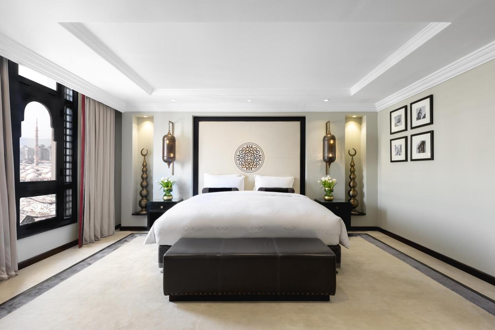 Готель Sofitel Shahd Al Madinah Medina Екстер'єр фото The photo shows a modern and stylish bedroom. It features a large bed with white linens, placed against a decorative wall with a circular design. On either side of the bed, there are elegant wall lamps illuminating the space. The room has a soft colo